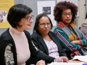 Three women sit at a table, one is addressing the audience