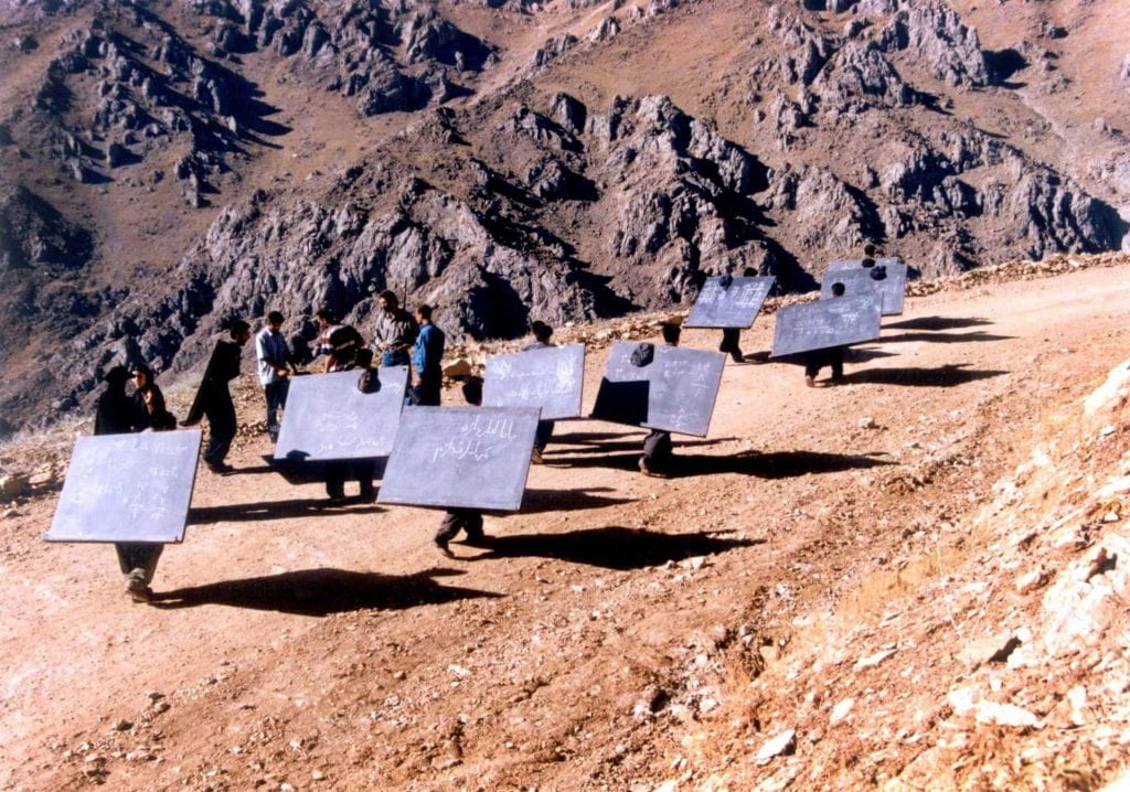 Men carrying large blackboards on their backs up a mountain path