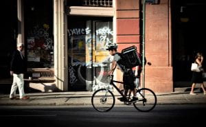 Man rides a bicycle carrying a large bag containing a food delivery