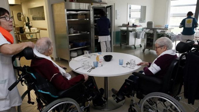 Two elderly people in wheelchairs sit at a table waiting to be served